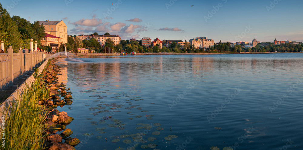 Obraz premium A wonderful panoramic view of a beautiful lake, embankment with a castle, silhouette of a church and city buildings on the background of the evening sky, Ternopil, Ukraine.