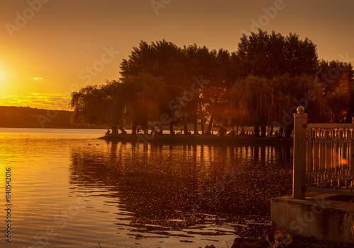 beautiful embankment of the pond with silhouettes of trees on an island in th...