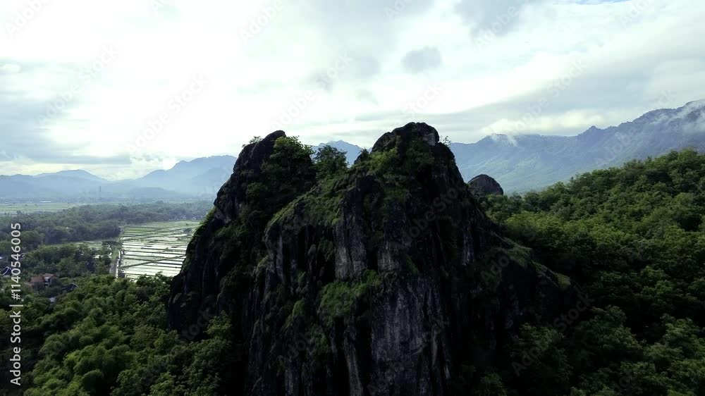 aerial view of ancient limestone rocky mountains, cliffs, and green trees with morning mist surrounded by rice fields. towering rocky hill of Sepikul mountain in Indonesia. aerial view of ancient limestone rocky mountains, cliffs, and green trees with morning mist surrounded by rice fields. towering rocky hill of Sepikul mountain in Indonesia.