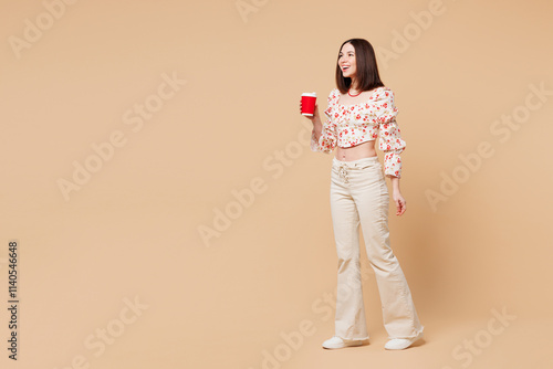 Full body young happy smiling woman wear white top casual clothes hold takeaway delivery craft paper cup coffee to go isolated on plain pastel light beige background studio portrait Lifestyle concept photo