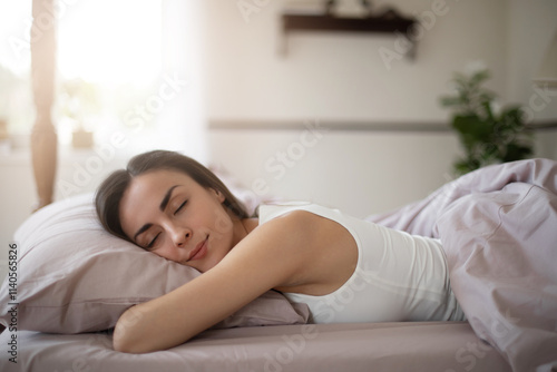 A young woman sleeps peacefully on a soft bed, her head resting on pillow wrapped in cozy lavender sheets.The bright calm bedroom exudes serenity and relaxation. Perfect for sleep or wellness themes