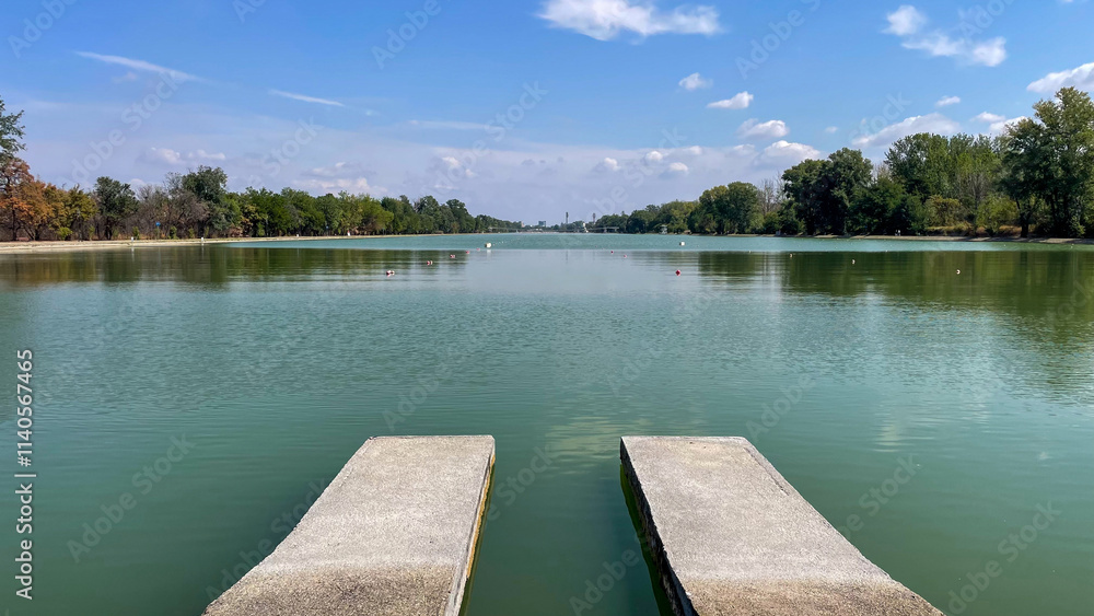 Naklejka premium Concrete piers extending into a calm green lake under a clear blue sky, perfect for themes of nature, relaxation, and travel destinations.