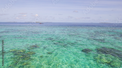 Obraz na płótnie Turquoise clear ocean water. The reef is visible under the water. In the distance there is a hydroplane pad, islands and white clouds. The gradient of the water shimmers from light blue to dark w salonie