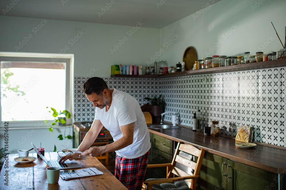 Man managing bills with laptop on kitchen desk Man managing bills with laptop on kitchen desk