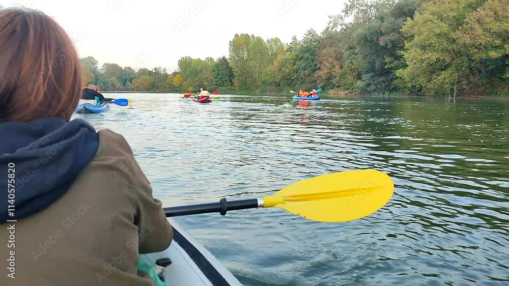 Woman sitting in an inflatable boat and rowing an oar, floating on the river with other people in boats on an autumn day. Many trees on banks. Kayaking tourism travel sport entertainment rest relax Woman sitting in an inflatable boat and rowing an oar, floating on the river with other people in boats on an autumn day. Many trees on banks. Kayaking tourism travel sport entertainment rest relax