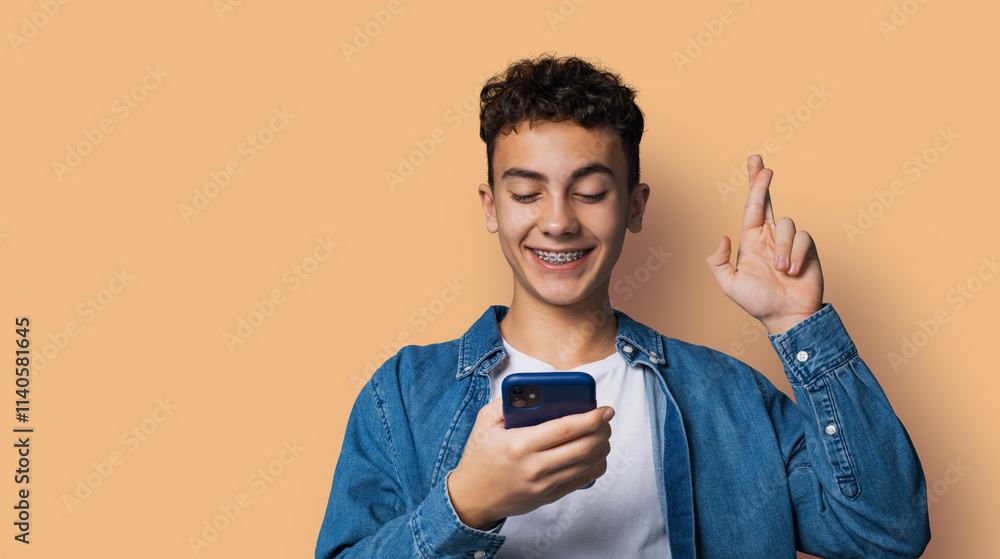 Smiling black curly hair funny man wear braces holding typing look read cell phone cellular smartphone cellphone, cross fingers, praying hope for good luck, isolate pastel plain beige brown background Smiling black curly hair funny man wear braces holding typing look read cell phone cellular smartphone cellphone, cross fingers, praying hope for good luck, isolate pastel plain beige brown background