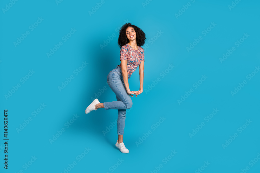Young woman in a colorful patterned t-shirt and jeans, posing against a vibrant blue background, embodies casual elegance and joy Young woman in a colorful patterned t-shirt and jeans, posing against a vibrant blue background, embodies casual elegance and joy