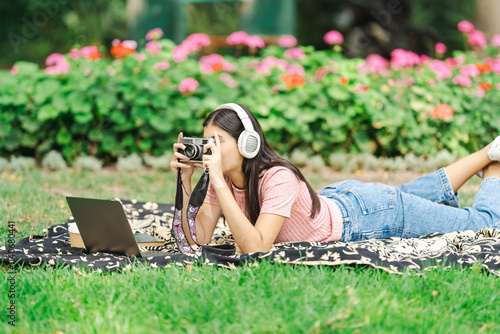 Young photographer taking pictures while lying in the garden with laptop and book