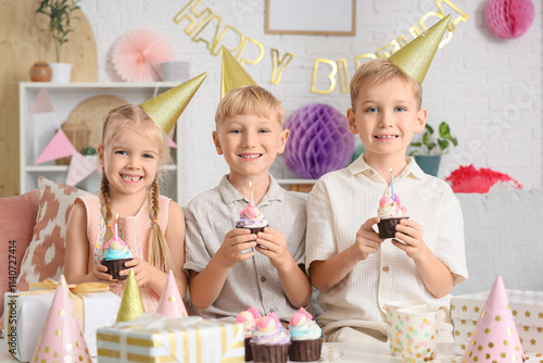 Cute little happy kids in party hats with cupcakes and gift boxes celebrating...