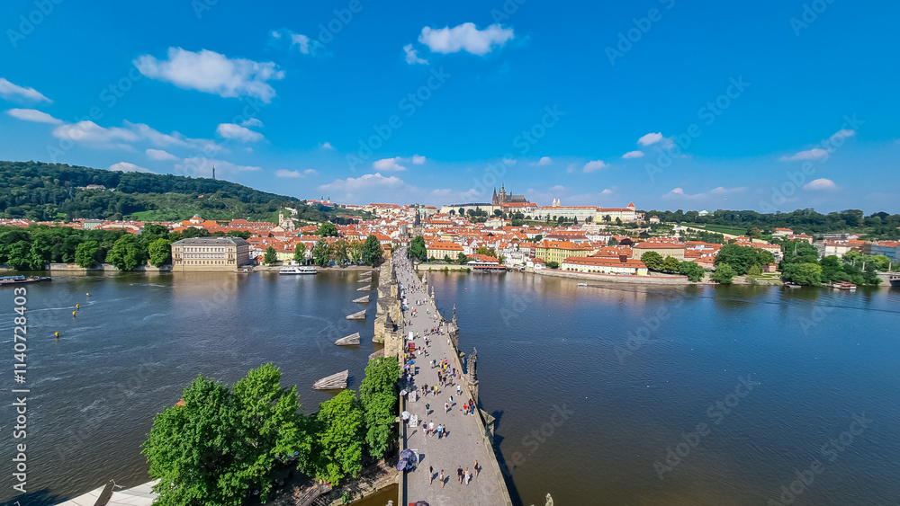 Fototapeta premium Panoramic view of iconic Charles Bridge stretches across the Vltava River in Prague, Czechia. Lined with statues and bustling with tourists. Prague Castle and St. Vitus historic Old Town in distance
