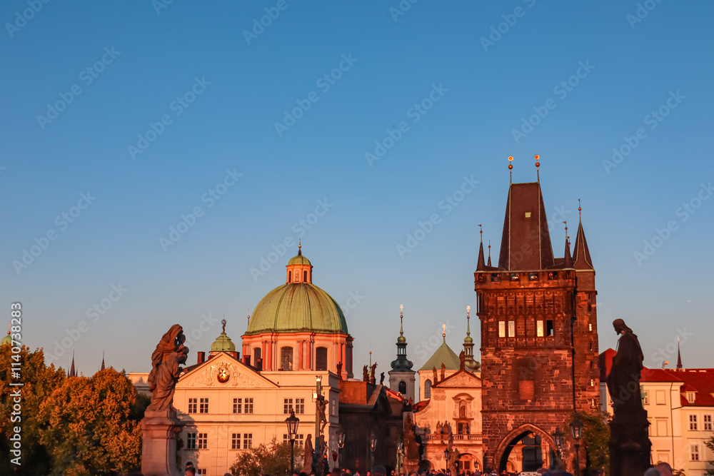 Fototapeta premium Sunset view from iconic Charles Bridge in Old Town Prague, Czechia. Gothic Old Town Bridge Tower with golden hour light. Baroque dome of the Church of St. Francis of Assisi in background. Tourism