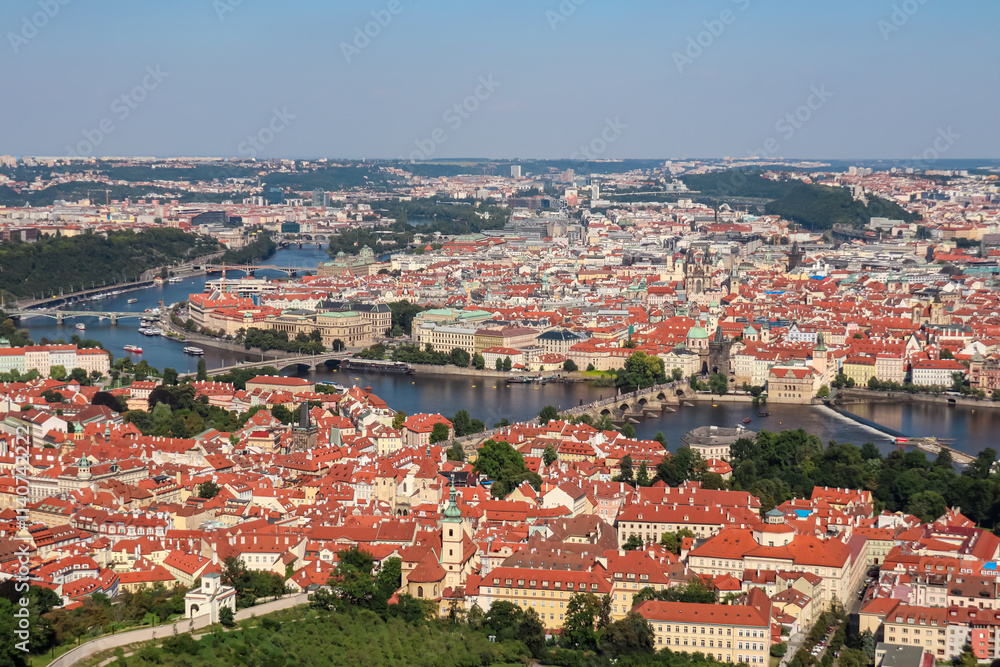 Aerial view of Prague seen from Petrin tower, Czechia. City's iconic landmark Charles Bridge is visible in distance. Vltava River winds through city. Historic city center with its red-tiled roofs Aerial view of Prague seen from Petrin tower, Czechia. City's iconic landmark Charles Bridge is visible in distance. Vltava River winds through city. Historic city center with its red-tiled roofs