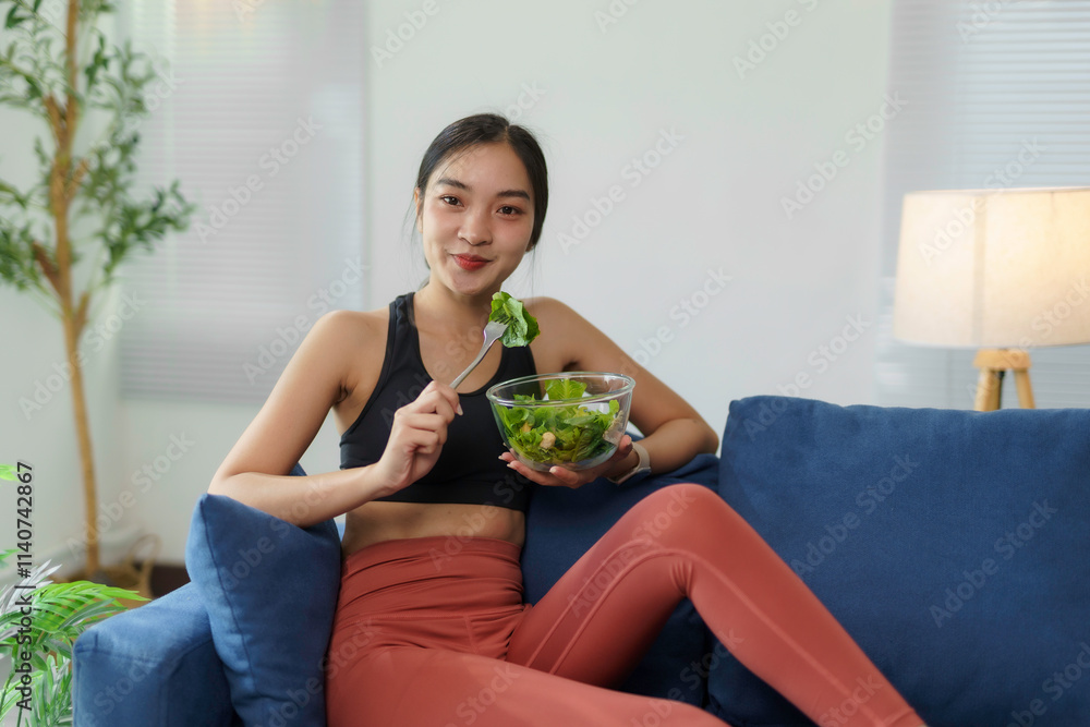 Young asian sportswoman enjoying healthy meal of fresh salad on comfortable sofa in living room, promoting healthy lifestyle and post workout nutrition Young asian sportswoman enjoying healthy meal of fresh salad on comfortable sofa in living room, promoting healthy lifestyle and post workout nutrition