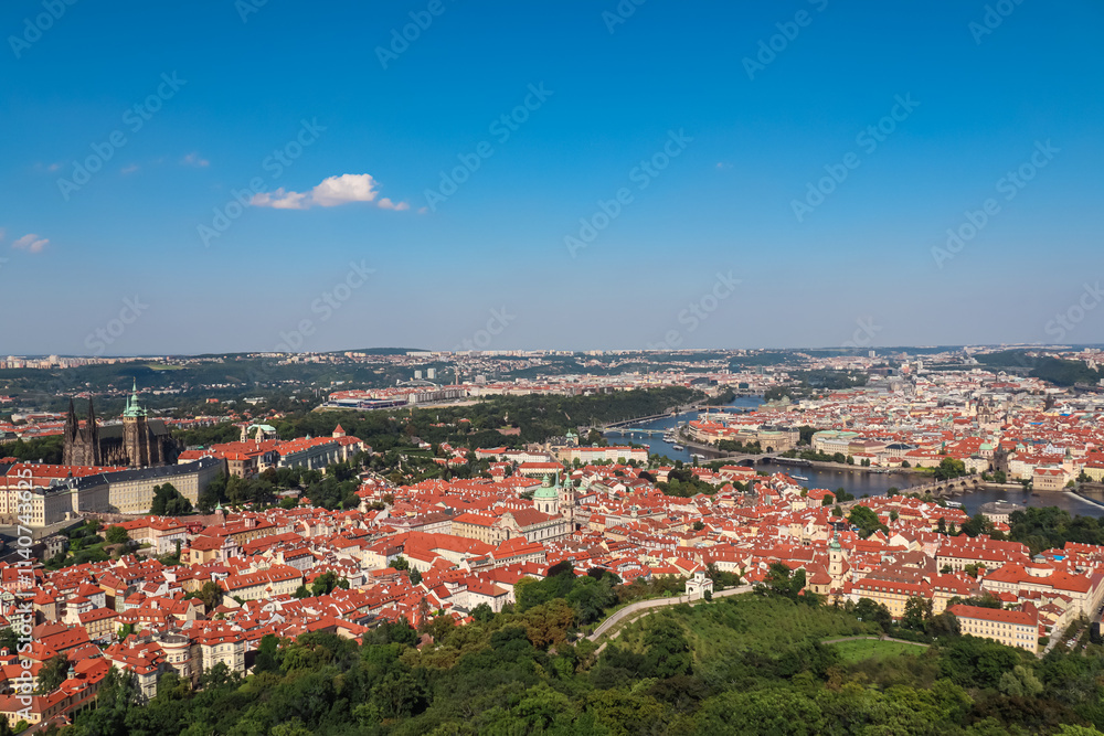 Fototapeta premium Aerial view of Prague seen from Petrin tower, Czechia. City's iconic landmarks, including Prague Castle, St. Vitus Cathedral and Charles Bridge are visible in distance. Vltava River winds through city