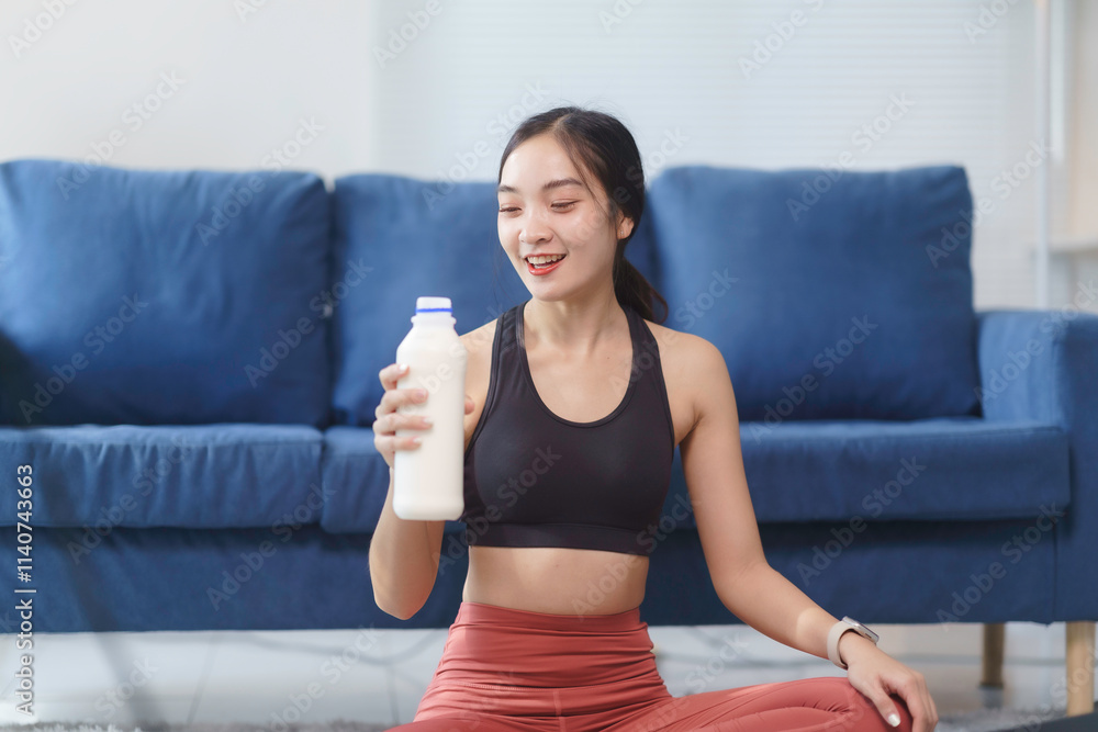Fit asian sportswoman smiling and holding a bottle of protein drink after exercising at home, promoting healthy lifestyle Fit asian sportswoman smiling and holding a bottle of protein drink after exercising at home, promoting healthy lifestyle