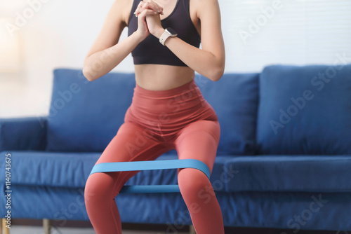 Athletic woman doing squats with a resistance band in her living room, focusing on her fitness routine