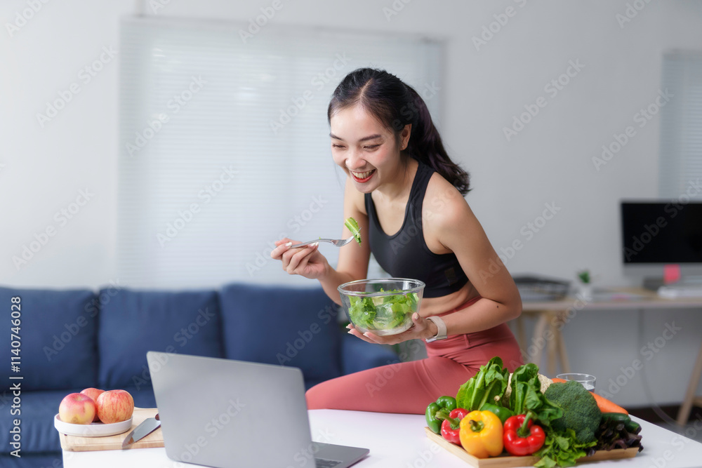Happy asian sportswoman eating healthy vegetable salad and having video call using laptop in the kitchen Happy asian sportswoman eating healthy vegetable salad and having video call using laptop in the kitchen