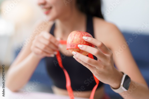 Woman holding and measuring a red apple with a red measuring tape, promoting healthy eating habits and weight management photo