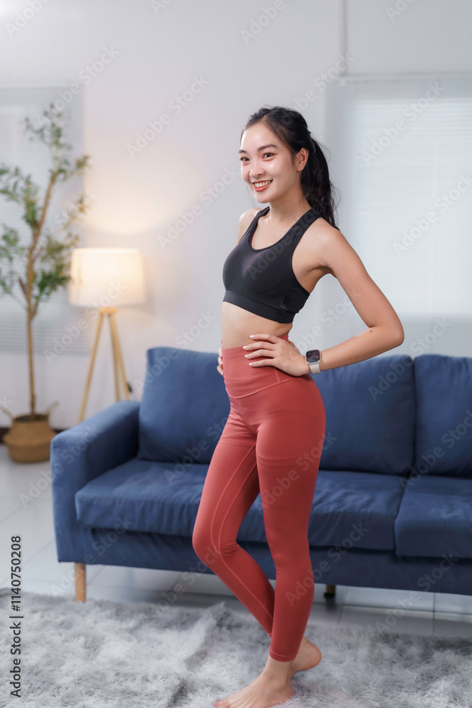Obraz premium Fit asian woman wearing sportswear standing in her living room, promoting a healthy and active lifestyle