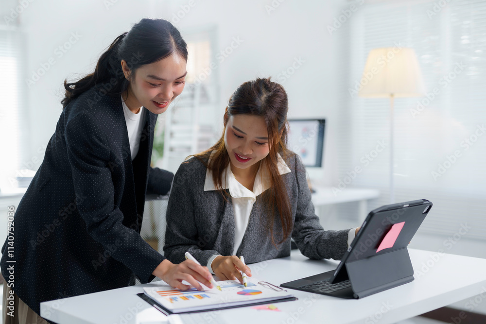 Two smiling asian businesswomen analyzing financial charts and data using a digital tablet and paperwork during a productive meeting in a modern office Two smiling asian businesswomen analyzing financial charts and data using a digital tablet and paperwork during a productive meeting in a modern office