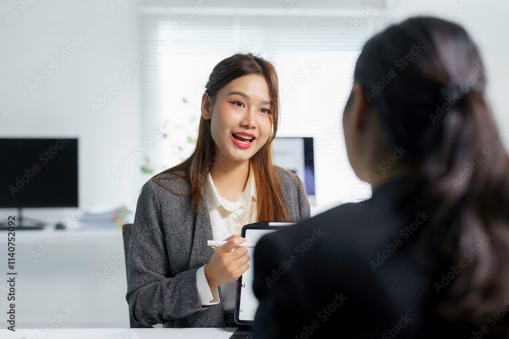 Two asian businesswomen are discussing a project, using a tablet to share ideas and information in a bright modern office Two asian businesswomen are discussing a project, using a tablet to share ideas and information in a bright modern office