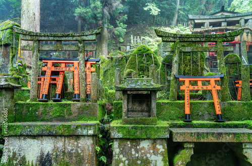 Small shinto place of worship with Torii Gates and inscriptioned stones at Fushimi Inari Taisha temple in Kyoto, Japan. ( Japanese inscriptions translated are different religion blessings) photo