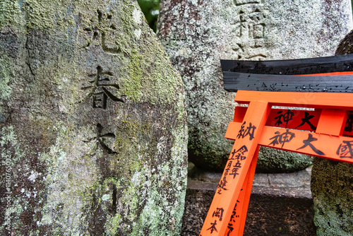 Small shinto place of worship with Torii Gates and inscriptioned stones at Fushimi Inari Taisha temple in Kyoto, Japan. ( Japanese inscriptions translated are different religion blessings) photo