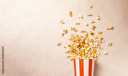 Popcorn explosion in red and white striped box on neutral background with copy space. Perfect for concepts related to movie nights, cinema snacks, entertainment, fun food, and party themes. photo