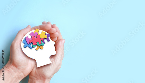 Hands holding paper head with jigsaw puzzle, Autism spectrum disorder family support concept, World Autism Awareness Day