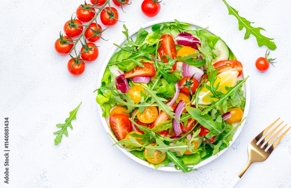 Vegan vegetable salad with red and yellow tomatoes, cucumber, red onion, green lettuce and arugula. White background, top view Vegan vegetable salad with red and yellow tomatoes, cucumber, red onion, green lettuce and arugula. White background, top view