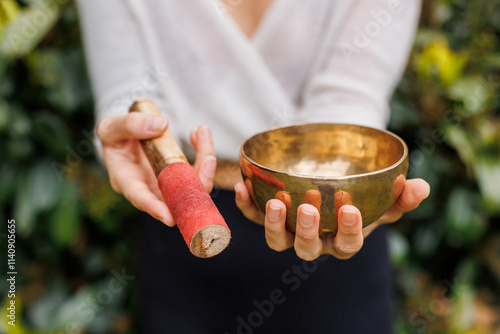 Close-up of a Tibetan singing bowl, held delicately with a red-tipped striker. Common in sound healing, the bowl produces meditative tones that promote focus and inner peace