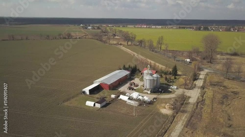 The view from the height of a large farm located among the green hilly fields. Video from a drone or a quadro. Agro-industrial complex with stainless steel silo. Organic food production.Dairy industry