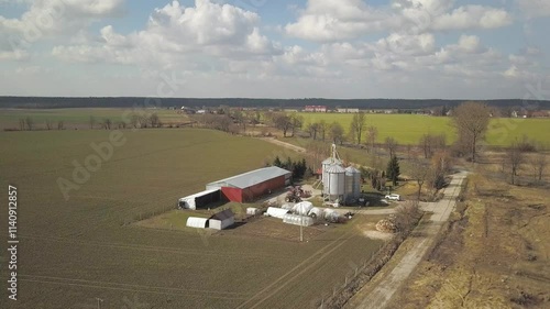 The view from the height of a large farm located among the green hilly fields. Video from a drone or a quadro. Agro-industrial complex with stainless steel silo. Organic food production.Dairy industry