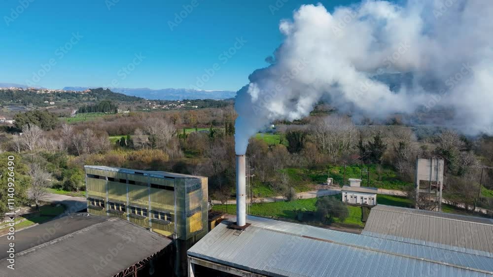 Aerial view of a processing plant emitting smoke, surrounded by fields and a rural landscape. Aerial view of a processing plant emitting smoke, surrounded by fields and a rural landscape.