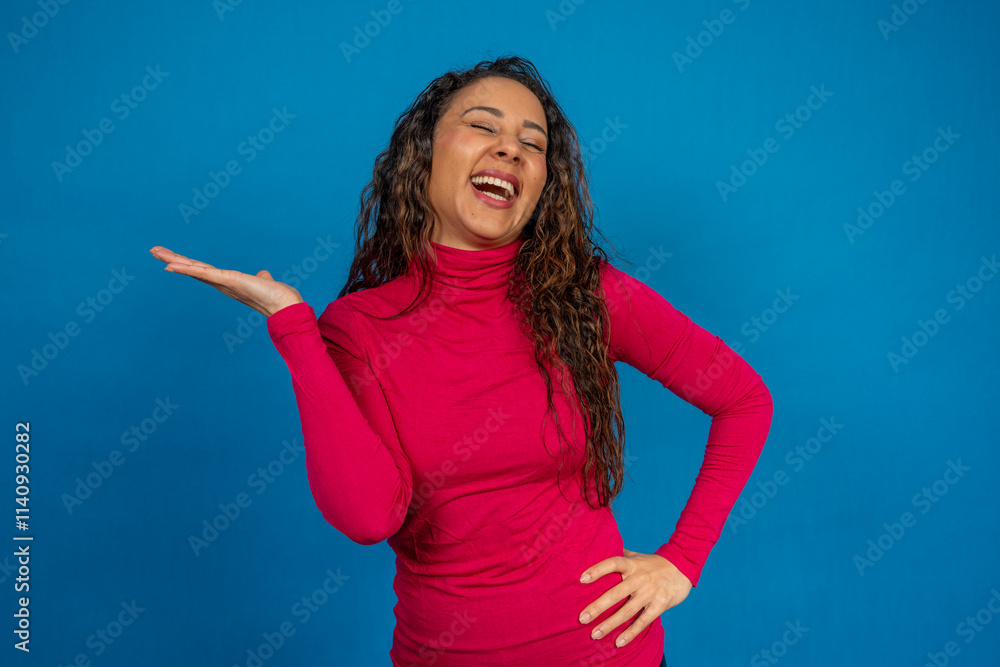 Young woman showing something and laughing on blue background Young woman showing something and laughing on blue background