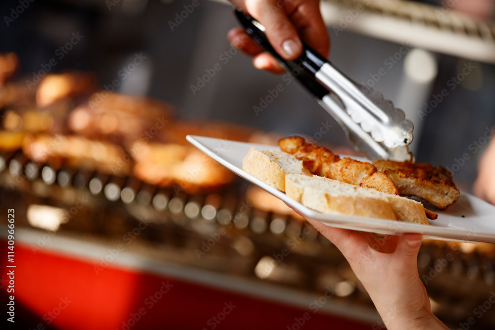 Grilled skewers with bread are being served. A hand holds a plate of food. Grilled skewers with bread are being served. A hand holds a plate of food.