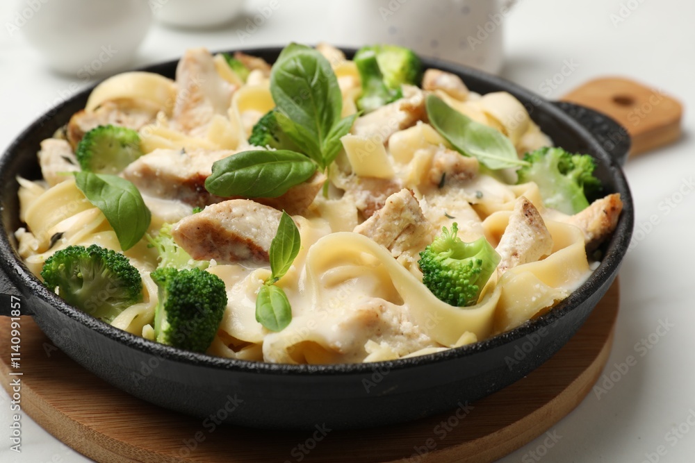 Delicious pasta Alfredo with chicken, cheese, creamy sauce, broccoli and basil on white table, closeup Delicious pasta Alfredo with chicken, cheese, creamy sauce, broccoli and basil on white table, closeup