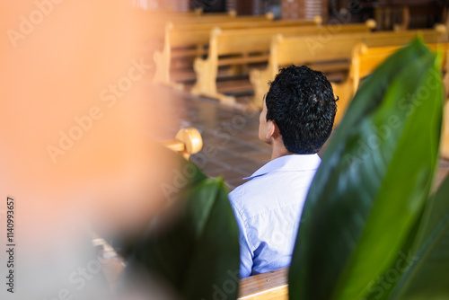 Man sitting with his back turned on a wooden chair in a temple, praying. The other chairs are empty during Holy Week photo