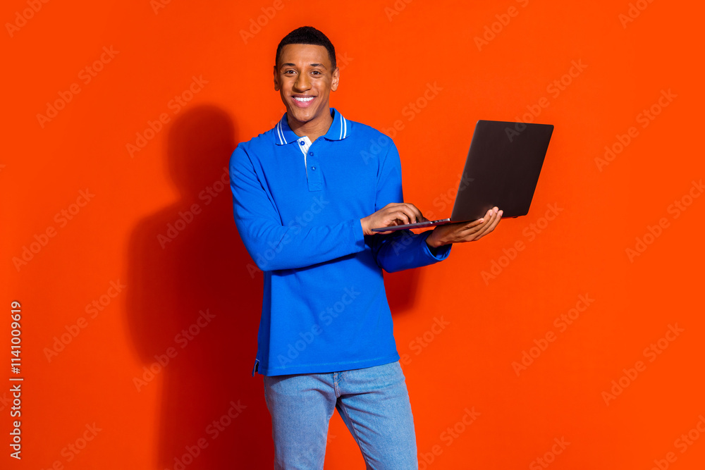 Stylish young man using laptop against vibrant orange background Stylish young man using laptop against vibrant orange background