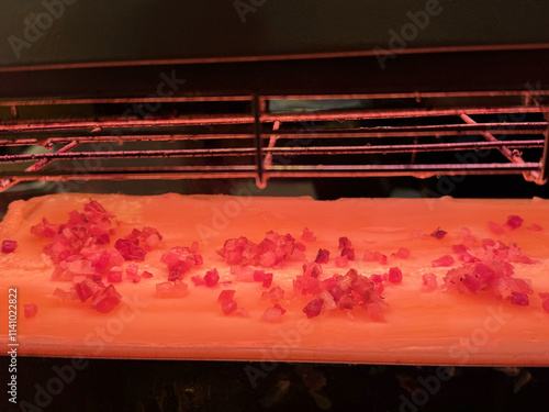 Pink himalayan salt block with diced red onions grilled under heat lamp photo