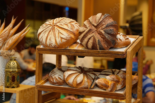 An inviting array of artisan breads, including beautifully crafted loaves and rolls, presented on a rustic wooden rack, surrounded by the warm ambiance of a bustling bakery