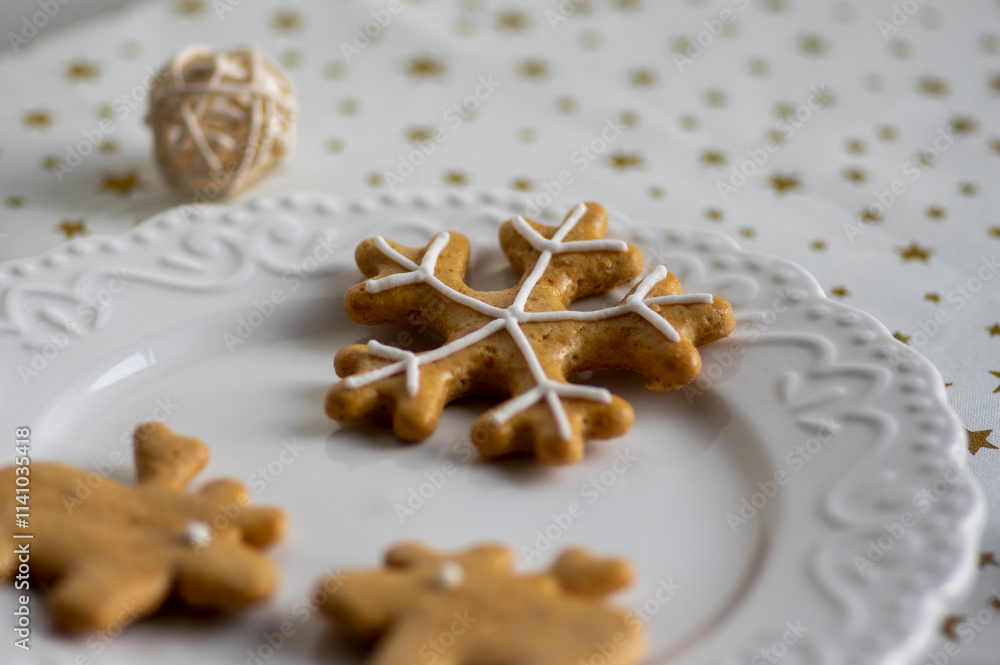 Painted traditional Christmas gingerbreads arranged on white plate, tablecloth with golden stars, snowflake and reindeer shapes Painted traditional Christmas gingerbreads arranged on white plate, tablecloth with golden stars, snowflake and reindeer shapes
