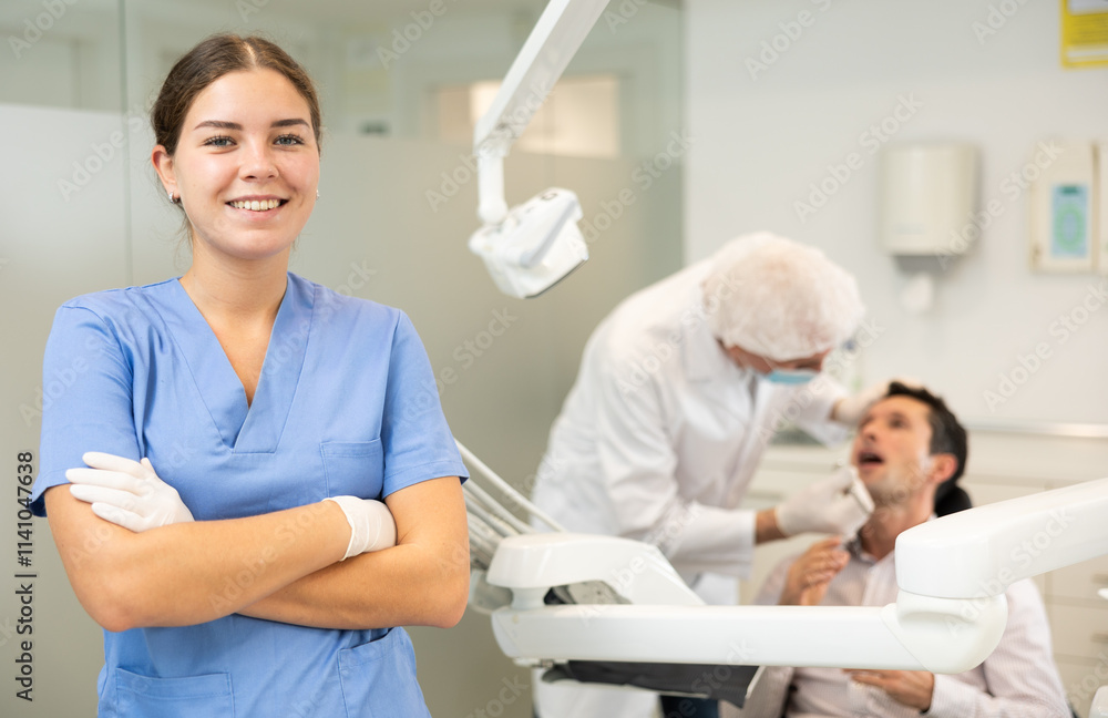 Young woman nurse in blue suit uniform is standing in dental office, clinic employee in suit uniform near dentists workplace. Doctor enjoys working in profession. Young woman nurse in blue suit uniform is standing in dental office, clinic employee in suit uniform near dentists workplace. Doctor enjoys working in profession.
