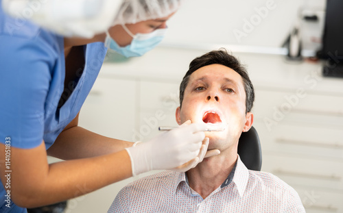 Man is sitting in armchair during dental diagnosis at dentist appointment. Girl doctor conducts examination procedure, identifies problem areas and tests sensitivity of teeth photo