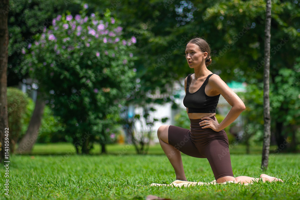 Fitness instructor showcasing kneeling hip flexor stretch on mat in lush green park. Sunlight filters through trees, creating serene outdoor atmosphere for wellness and flexibility Fitness instructor showcasing kneeling hip flexor stretch on mat in lush green park. Sunlight filters through trees, creating serene outdoor atmosphere for wellness and flexibility