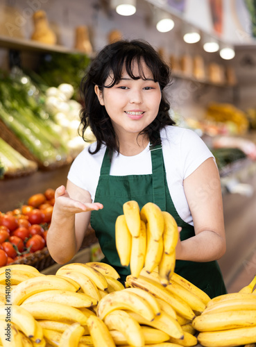 Friendly saleswoman puts fresh bananas on the supermarket shelves photo