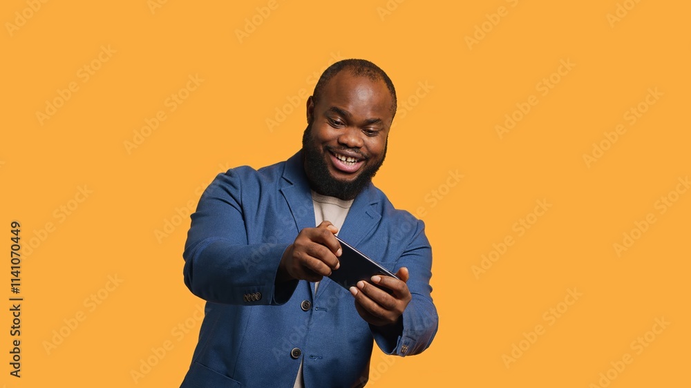 Happy man playing videogames on smartphone, celebrating after defeating foes, clenching hand gesture. Passionate BIPOC player thrilled about winning game on phone, studio background, camera A Happy man playing videogames on smartphone, celebrating after defeating foes, clenching hand gesture. Passionate BIPOC player thrilled about winning game on phone, studio background, camera A