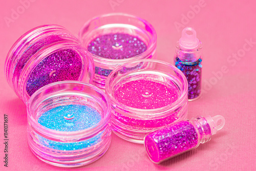 Collection of small plastic containers filled with various colors of glitter, on a pink surface. The vibrant and diverse colors of the glitter. Crafts, makeup, decoration concepts photo