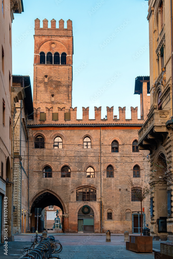 Fototapeta premium Narrow street in Bologna old town, Emilia Romagna, Italy, featuring historic architecture and the iconic Palazzo del Podesta at sunrise with nobody. Vertical orientation. Travel destination in Europe