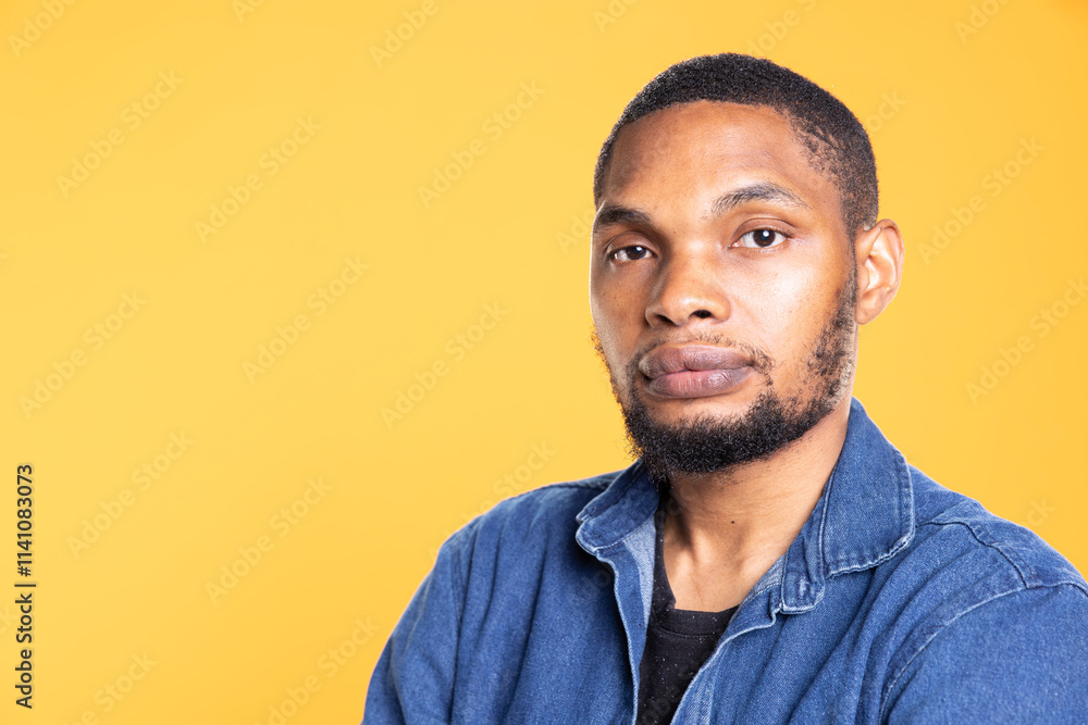 Obraz premium Portrait of african american serious man posing in front of the camera, standing with arms crossed against yellow background. Relaxed cool person feeling confident in studio.